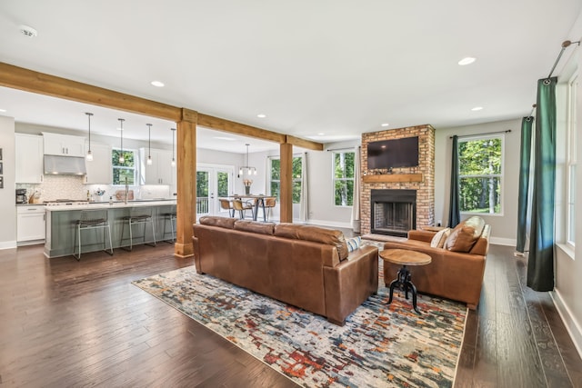 living room featuring an inviting chandelier, a wealth of natural light, a fireplace, and dark wood-type flooring