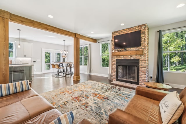 living room featuring a brick fireplace, beam ceiling, dark hardwood / wood-style floors, and a chandelier