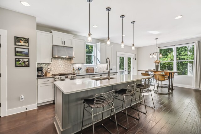 kitchen with white cabinets, a center island with sink, hanging light fixtures, and sink