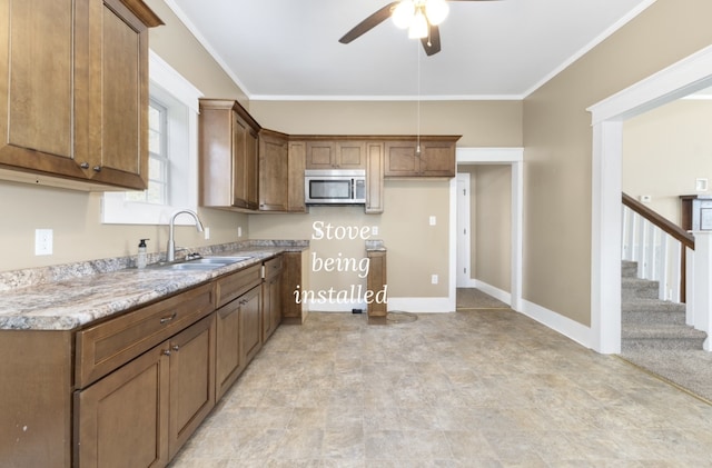 kitchen with ceiling fan, ornamental molding, light stone counters, and sink