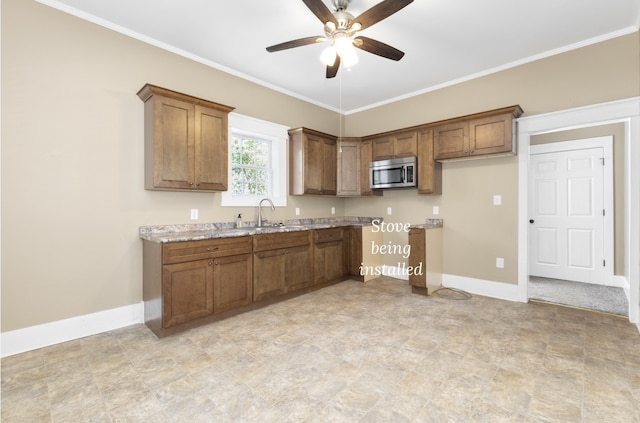 kitchen featuring ornamental molding, light stone countertops, ceiling fan, and sink