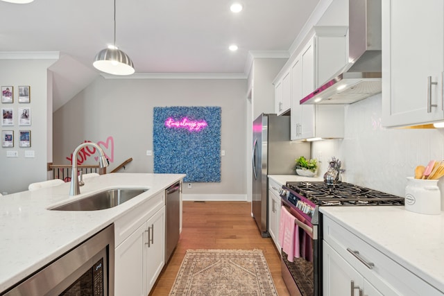 kitchen with sink, appliances with stainless steel finishes, wall chimney exhaust hood, hanging light fixtures, and light hardwood / wood-style flooring