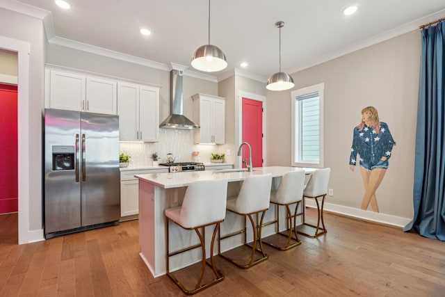 kitchen featuring stainless steel appliances, light hardwood / wood-style floors, white cabinetry, wall chimney exhaust hood, and a kitchen island with sink