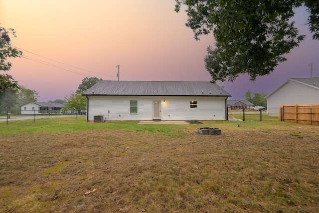 back house at dusk featuring central AC unit and a yard