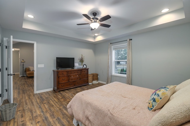 bedroom with ceiling fan, a tray ceiling, and dark hardwood / wood-style flooring