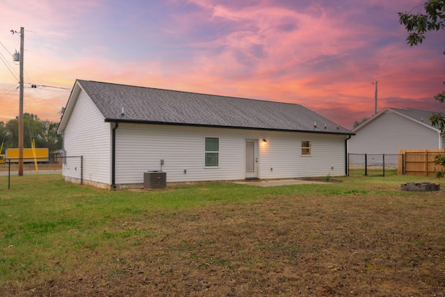 back house at dusk featuring cooling unit and a lawn