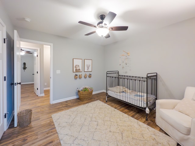 bedroom with ceiling fan, a crib, and dark hardwood / wood-style floors