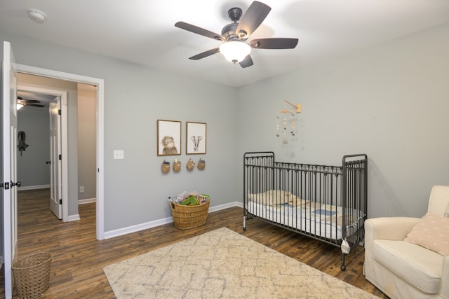 bedroom featuring ceiling fan, a nursery area, and dark wood-type flooring