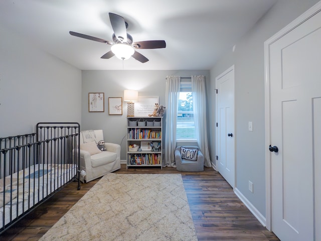 bedroom featuring a crib, ceiling fan, and dark wood-type flooring