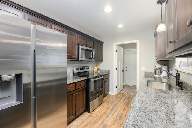 kitchen with appliances with stainless steel finishes, hanging light fixtures, light hardwood / wood-style floors, light stone counters, and sink