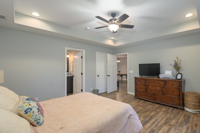 bedroom featuring a tray ceiling, ceiling fan, ensuite bathroom, and dark hardwood / wood-style flooring