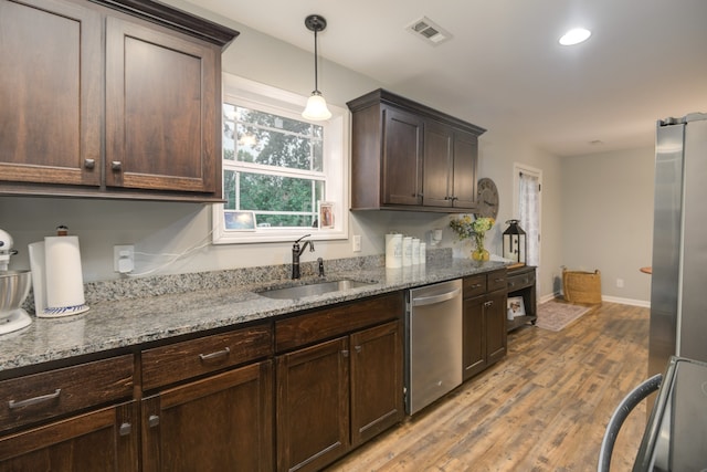 kitchen with light stone counters, pendant lighting, sink, stainless steel appliances, and light wood-type flooring