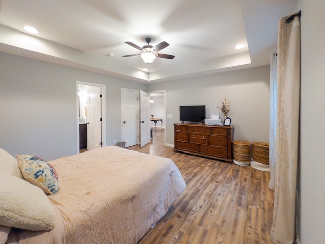 bedroom with ceiling fan, hardwood / wood-style flooring, a raised ceiling, and ensuite bathroom