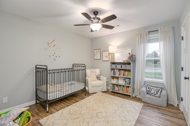 bedroom with ceiling fan, dark wood-type flooring, and a nursery area