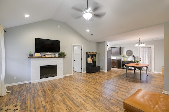 living room with ceiling fan with notable chandelier, vaulted ceiling, and dark hardwood / wood-style floors