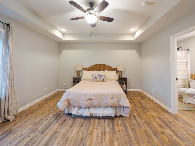 bedroom featuring hardwood / wood-style flooring, a raised ceiling, ensuite bathroom, and ceiling fan