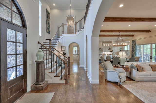 entryway featuring wood-type flooring, beam ceiling, a towering ceiling, and a notable chandelier