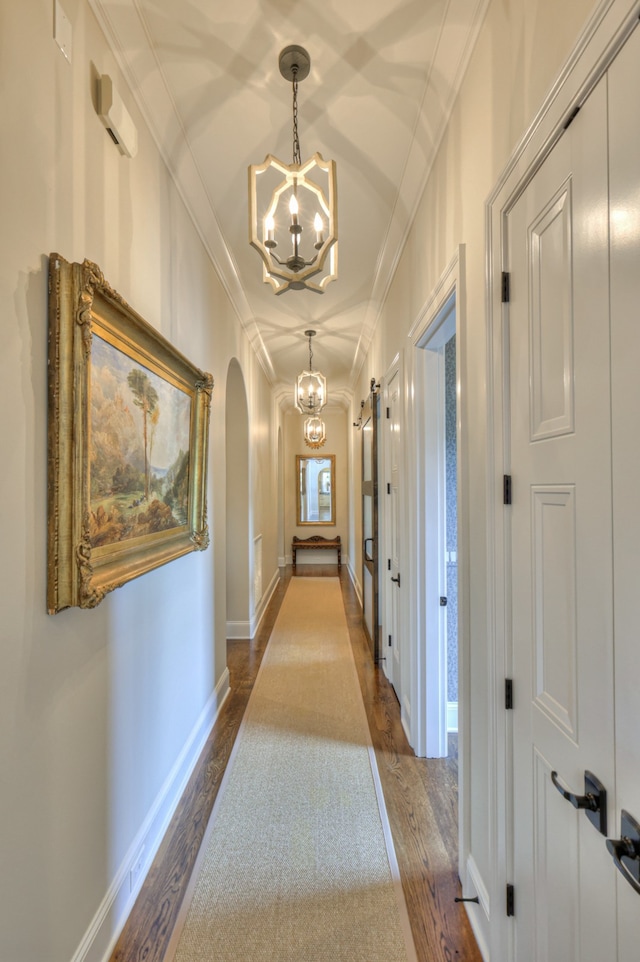 hallway with ornamental molding, wood-type flooring, and a chandelier