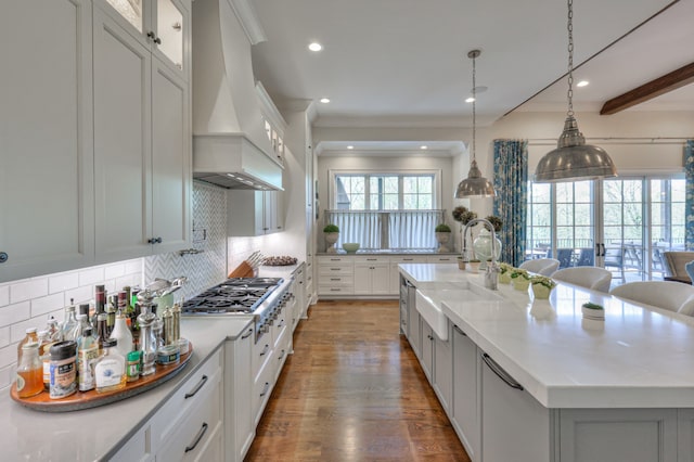 kitchen with a large island with sink, white cabinetry, stainless steel gas cooktop, custom exhaust hood, and sink