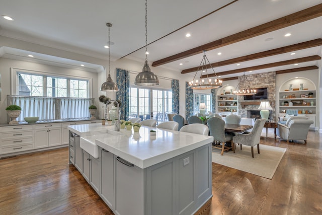 kitchen with a large island with sink, sink, a stone fireplace, decorative light fixtures, and dark hardwood / wood-style flooring