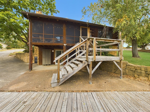 rear view of house featuring a deck, a sunroom, a lawn, and a patio