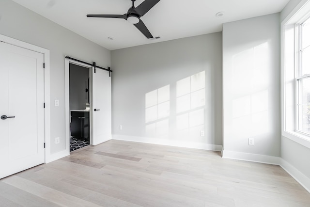 unfurnished bedroom featuring ceiling fan, light hardwood / wood-style floors, ensuite bath, and a barn door