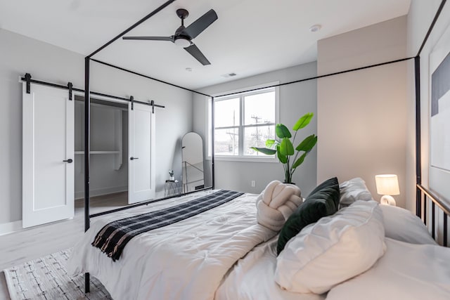 bedroom featuring a barn door, light wood-type flooring, and ceiling fan