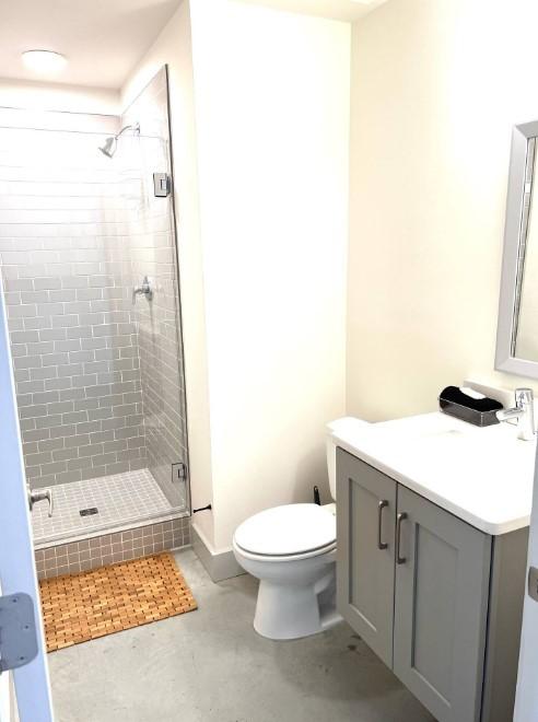 full bath featuring concrete flooring, toilet, a stall shower, and vanity