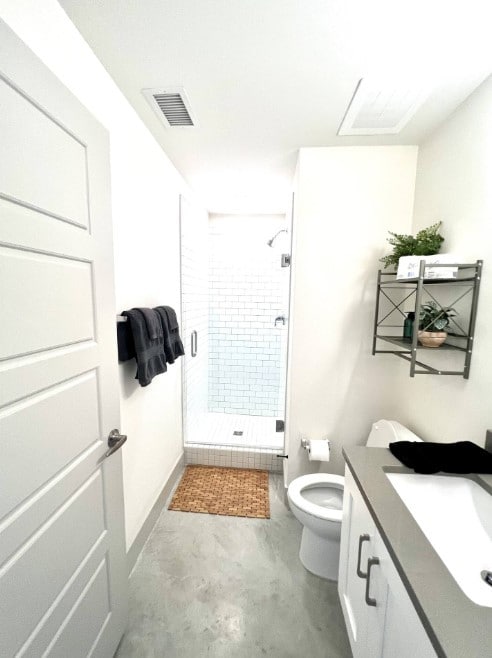 bathroom with vanity, a shower with shower door, toilet, and concrete floors