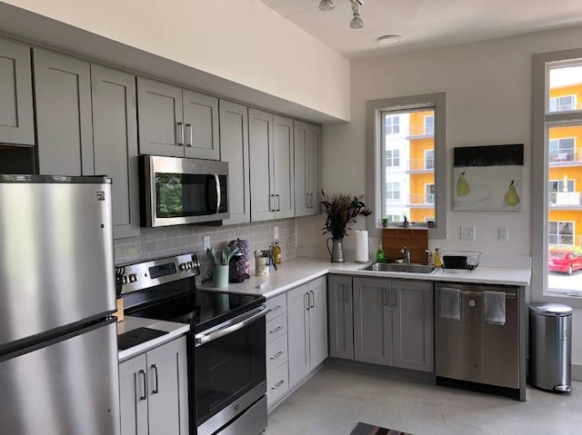 kitchen featuring gray cabinets, light countertops, a sink, tasteful backsplash, and appliances with stainless steel finishes