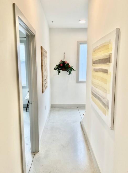hallway with baseboards, concrete floors, and plenty of natural light