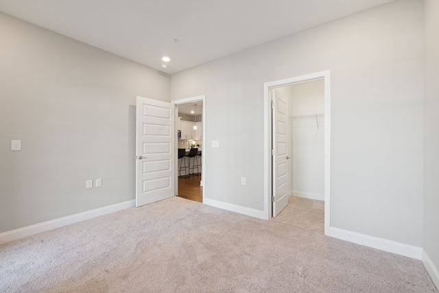 unfurnished bedroom featuring a spacious closet, light colored carpet, and a closet