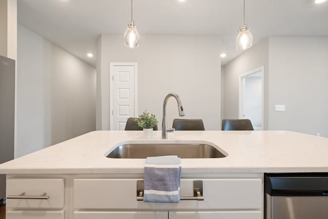 kitchen featuring light stone counters, sink, white cabinetry, hanging light fixtures, and a center island with sink