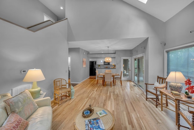 living room featuring an inviting chandelier, light hardwood / wood-style flooring, a skylight, and high vaulted ceiling