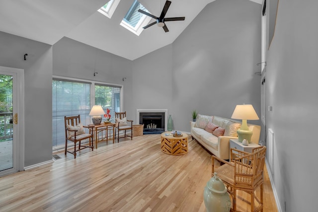 living room featuring a healthy amount of sunlight, light hardwood / wood-style flooring, a skylight, and high vaulted ceiling