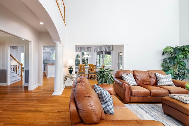 living room featuring wood-type flooring, a towering ceiling, and decorative columns