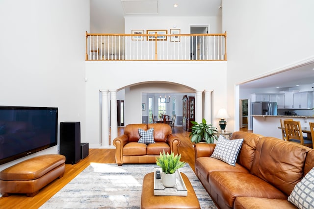 living room featuring light wood-type flooring, a towering ceiling, and ornate columns