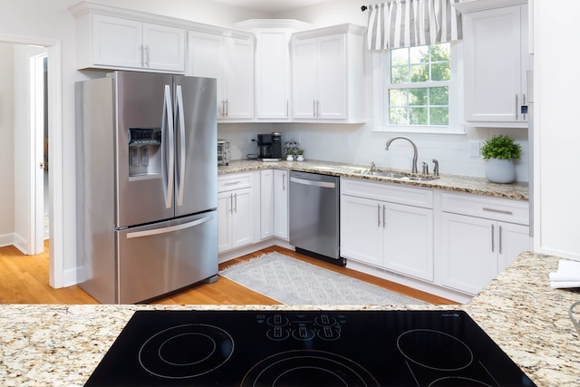 kitchen featuring light wood-type flooring, light stone counters, sink, white cabinets, and appliances with stainless steel finishes