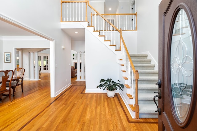 entryway with light wood-type flooring, a towering ceiling, and crown molding