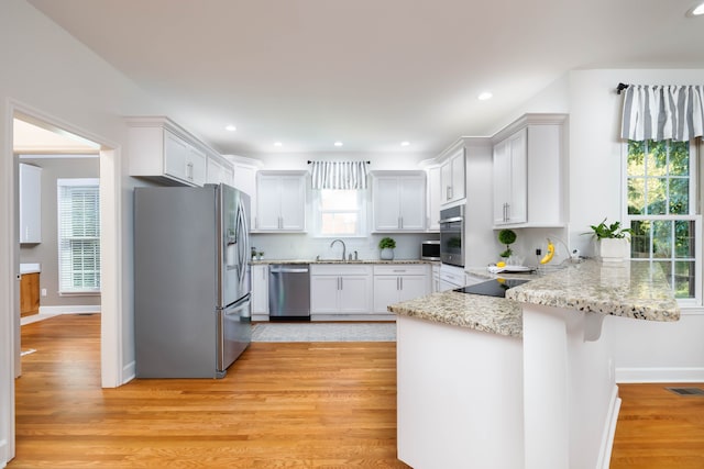 kitchen featuring light wood-type flooring, sink, white cabinets, kitchen peninsula, and appliances with stainless steel finishes