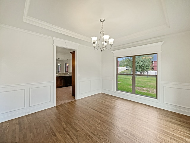 unfurnished room with a raised ceiling, ornamental molding, an inviting chandelier, and hardwood / wood-style flooring