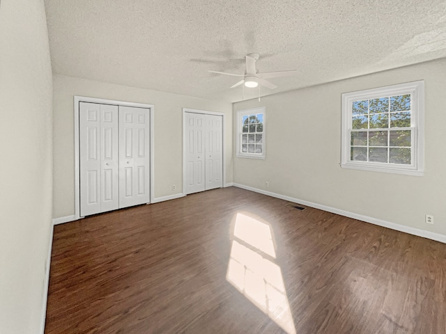 unfurnished bedroom featuring a textured ceiling, dark hardwood / wood-style floors, ceiling fan, and multiple closets