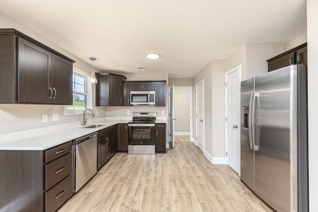 kitchen with appliances with stainless steel finishes, pendant lighting, sink, dark brown cabinets, and light wood-type flooring