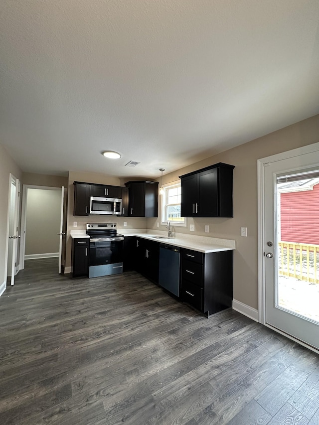 kitchen featuring dark cabinets, stainless steel appliances, light countertops, pendant lighting, and a sink