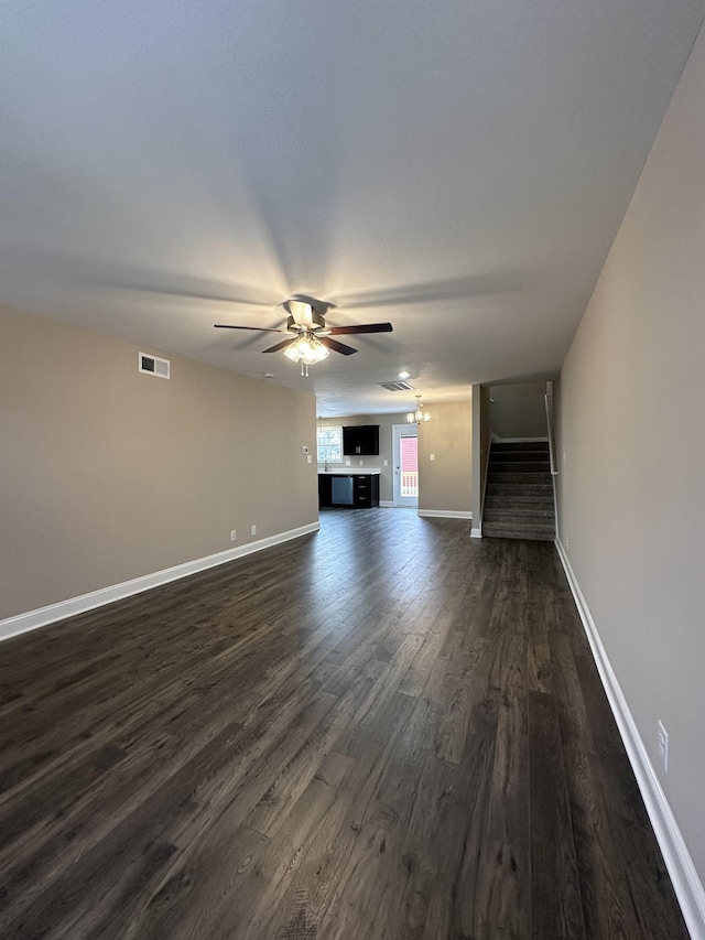 unfurnished living room featuring dark wood-style flooring, visible vents, a ceiling fan, baseboards, and stairs