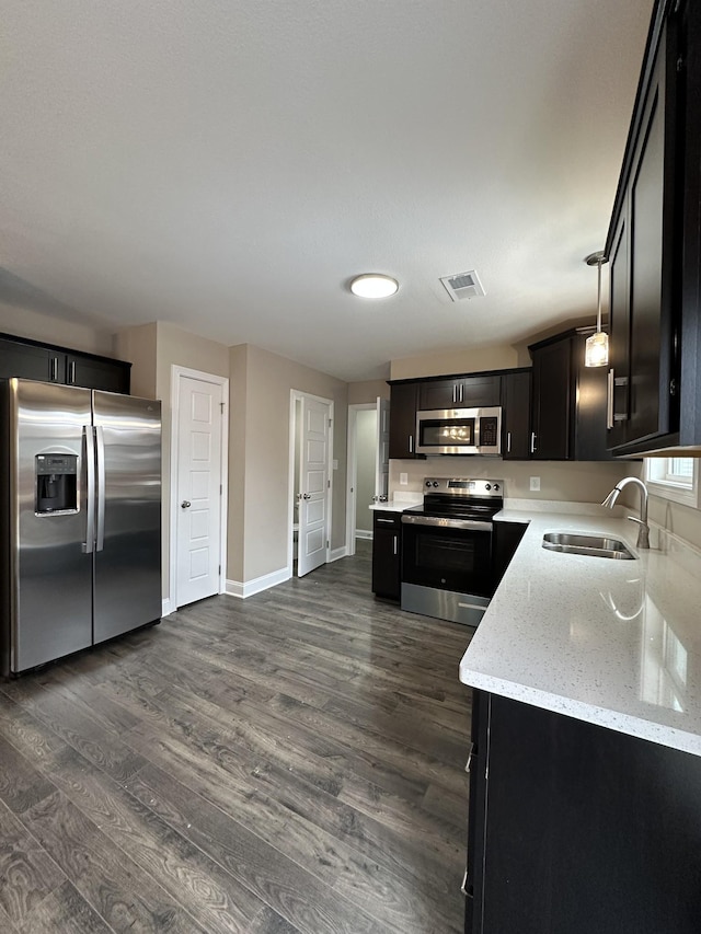 kitchen with light stone counters, hanging light fixtures, appliances with stainless steel finishes, a sink, and dark cabinets