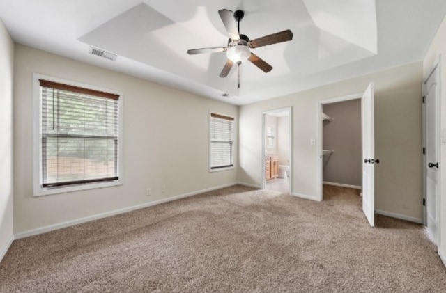 unfurnished bedroom with a closet, light colored carpet, ensuite bath, a spacious closet, and ceiling fan