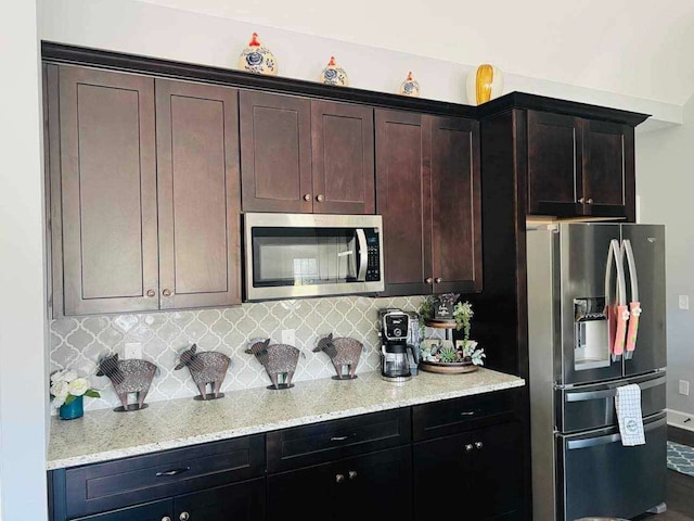 kitchen featuring dark brown cabinets, stainless steel appliances, decorative backsplash, and light stone countertops