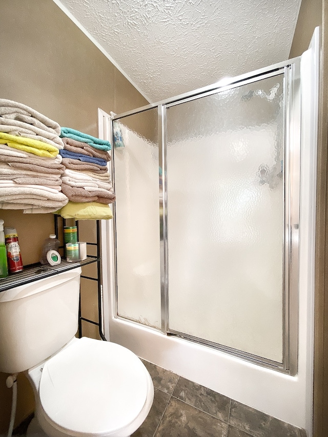 bathroom with a textured ceiling, toilet, and a shower with door