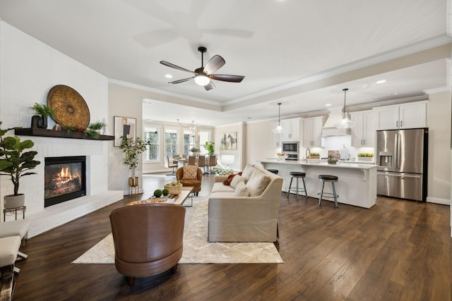 living room with dark wood-type flooring, sink, ceiling fan, ornamental molding, and a fireplace